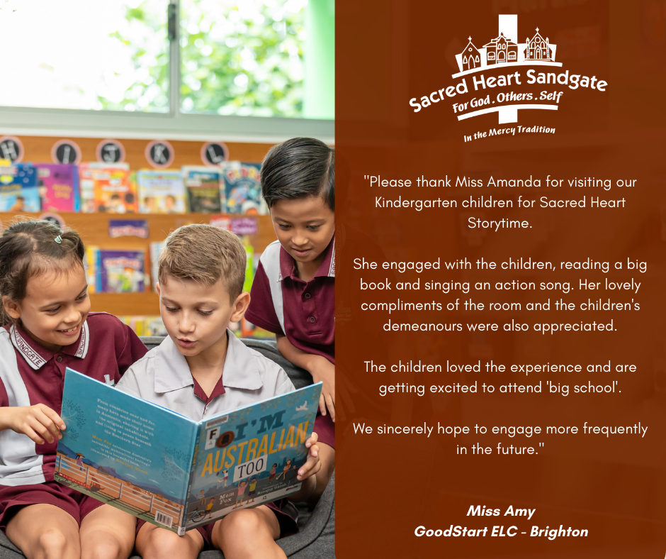 Three young Sacred Heart Sandgate students sit together on the floor, smiling and reading a large picture book during a kindergarten storytime session. They are wearing maroon and grey school uniforms and are closely engaged with the book. Indoor classroom resources and children’s books are visible in the background.